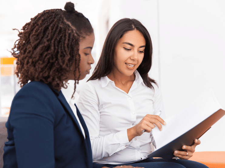 two young ladies looking at a document and talking